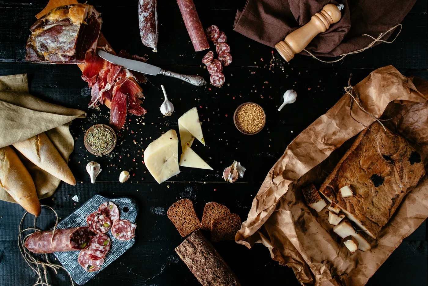 Tabla con jamón cortado, embutidos, queso y pan sobre una mesa oscura
